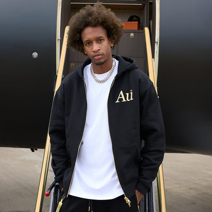 Person wearing a black hoodie with 'Au' logo in front of an airplane