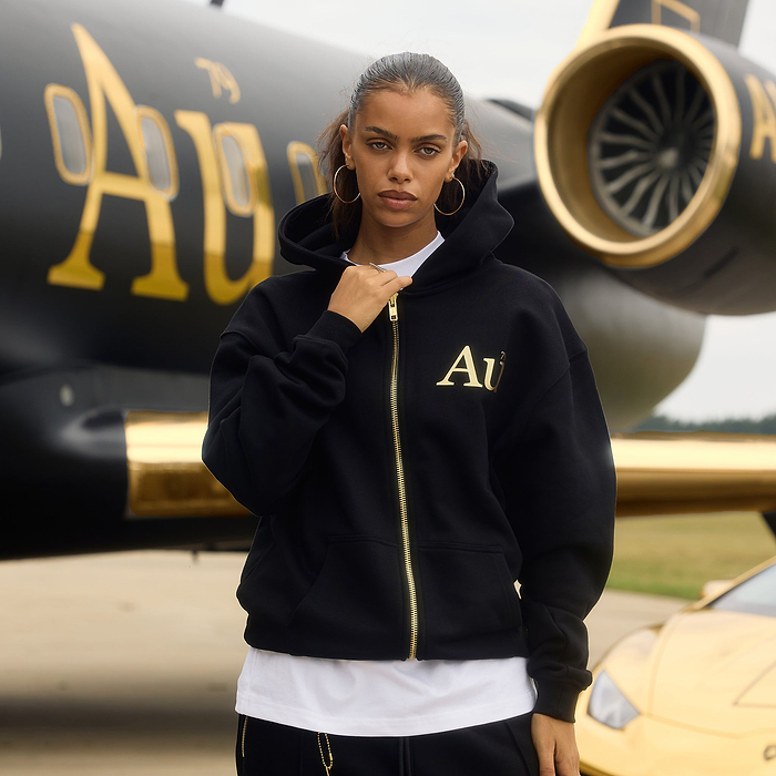 Person wearing a black hoodie with gold 'Au' lettering in front of jet.