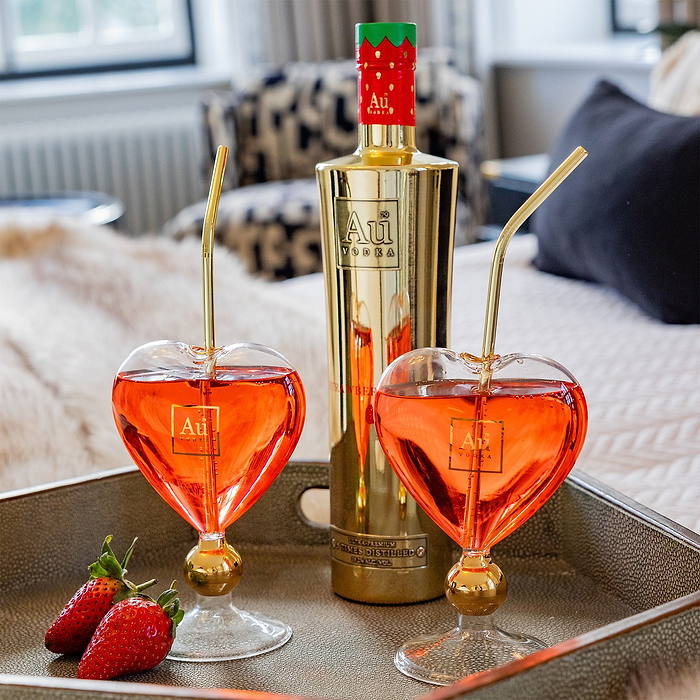 Gold bottle of Au Vodka  with two heart-shaped glasses filled with red vodka on.