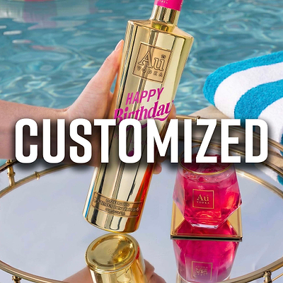 Hand holding a gold Au Vodka bottle with a pink label, next to a glass of pink drink on a gold tray