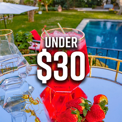 Red cocktail with strawberries and Au Vodka bottle on a mirrored tray, with text Under $30