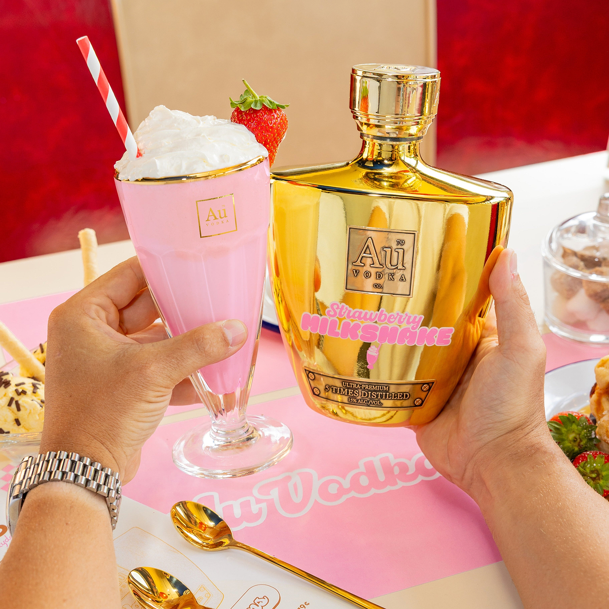 Au Vodka Strawberry Milkshake bottle and a matching pink milkshake in a glass held by hands