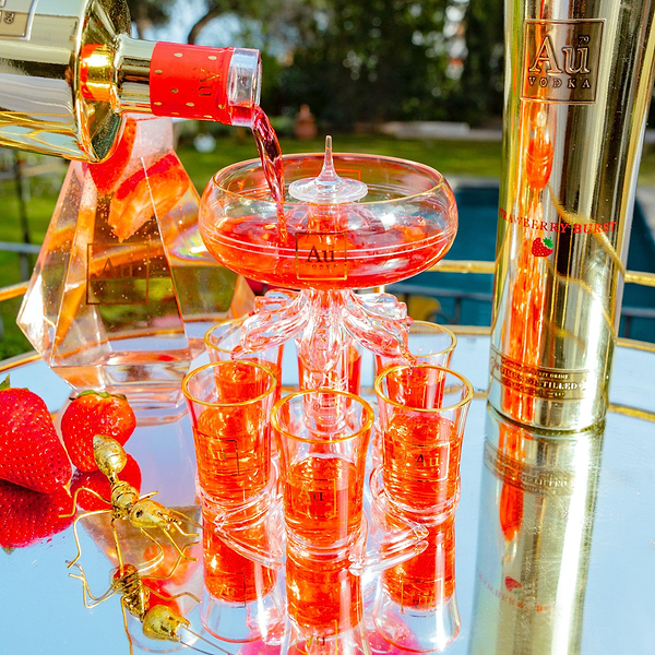 Au Vodka bottle pouring red liquid into a glass shot tower with fresh strawberries on a mirrored tray