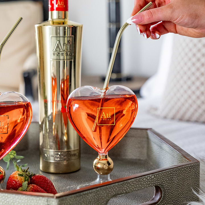 Au Vodka merchandise heart shaped glass with gold straw and red cocktail on a tray