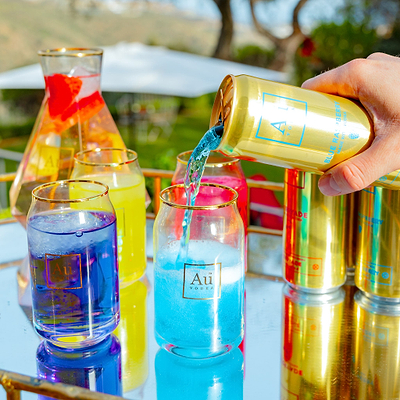 Au Vodka branded glassware being filled with blue raspberry drink from a gold can