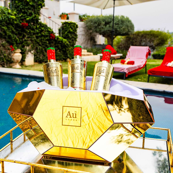 Three Au Vodka Red Cherry bottles in a gold diamond shaped ice bucket by a pool