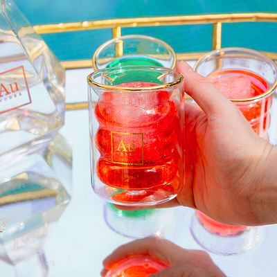Hand holding an Au Vodka branded glass with red cocktail and ice