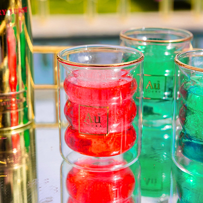 Au Vodka branded ripple glassware with gold rim on a reflective surface