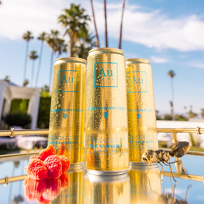 Three Au Vodka Blue Raspberry Soda cans on a tray with raspberries and an ant