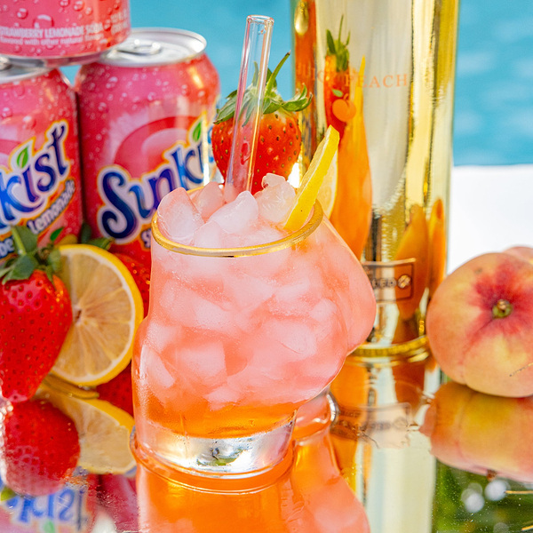 Au Vodka glassware filled with pink cocktail ice strawberry and lemon slice with Sunkist cans and gold bottle