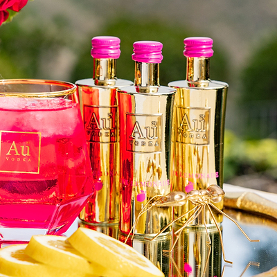Three Au Vodka USA Pink Lemonade bottles with a pink drink in a glass and lemon slices