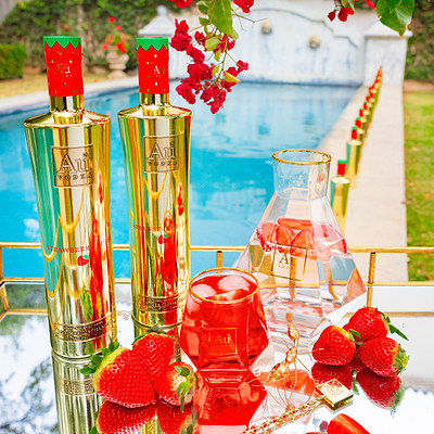 Two Au Vodka Strawberry Burst 750ml bottles, a glass of vodka, and a carafe with strawberries