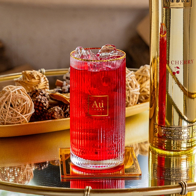 Au Vodka Red Cherry cocktail in a ribbed glass with ice next to a gold bottle on a mirrored tray