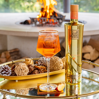 Au Vodka Juicy Peach bottle and cocktail in a branded glassware on a mirrored tray with decorative pinecones