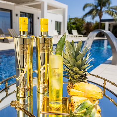 Au Vodka Pineapple Crush & Highrise Glass, filled with yellow liquid. on a poolside backdrop.