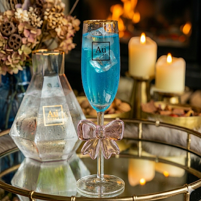Au Vodka branded champagne flute with a pink glass bow stem containing a blue cocktail with ice