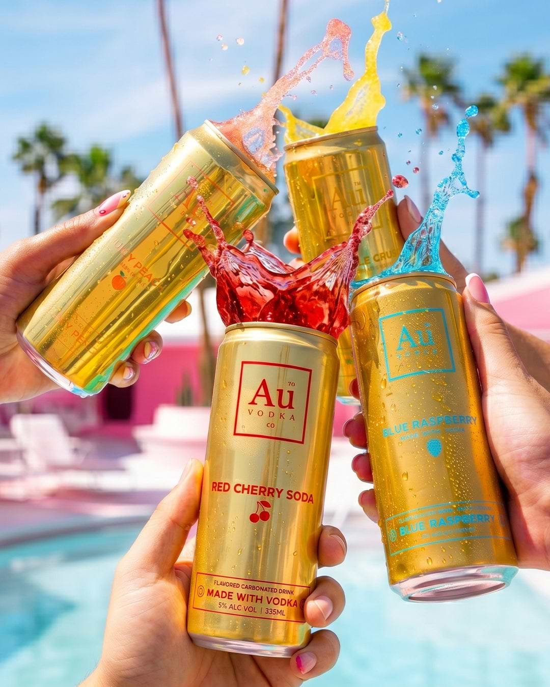 Four Au Vodka Co cans in Red Cherry Soda, Blue Raspberry, and Juicy Peach flavors with liquid splashing