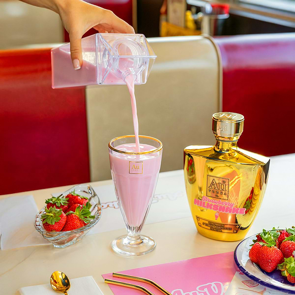Hand pouring pink cocktail from a clear carton into a glass next to Au Vodka bottle