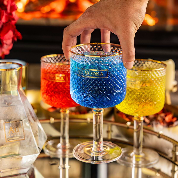 Hand holding a blue Au Vodka branded textured glass with red and yellow glasses on a tray