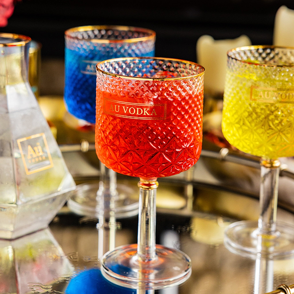 Au Vodka branded textured glassware filled with red blue and yellow cocktails on a reflective tray