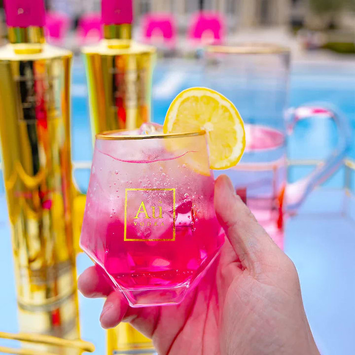 Hand holding a glass of pink Au Vodka cocktail with a lemon slice garnish