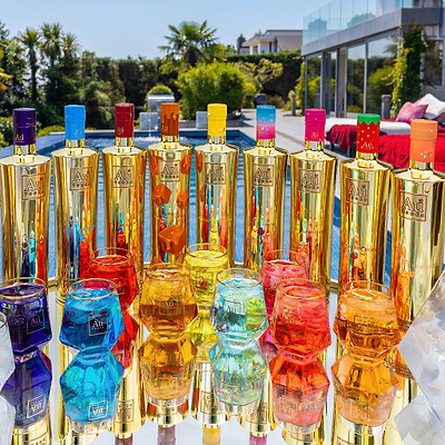 Au Vodka bottles in various colors with matching glasses, set outdoors by a pool