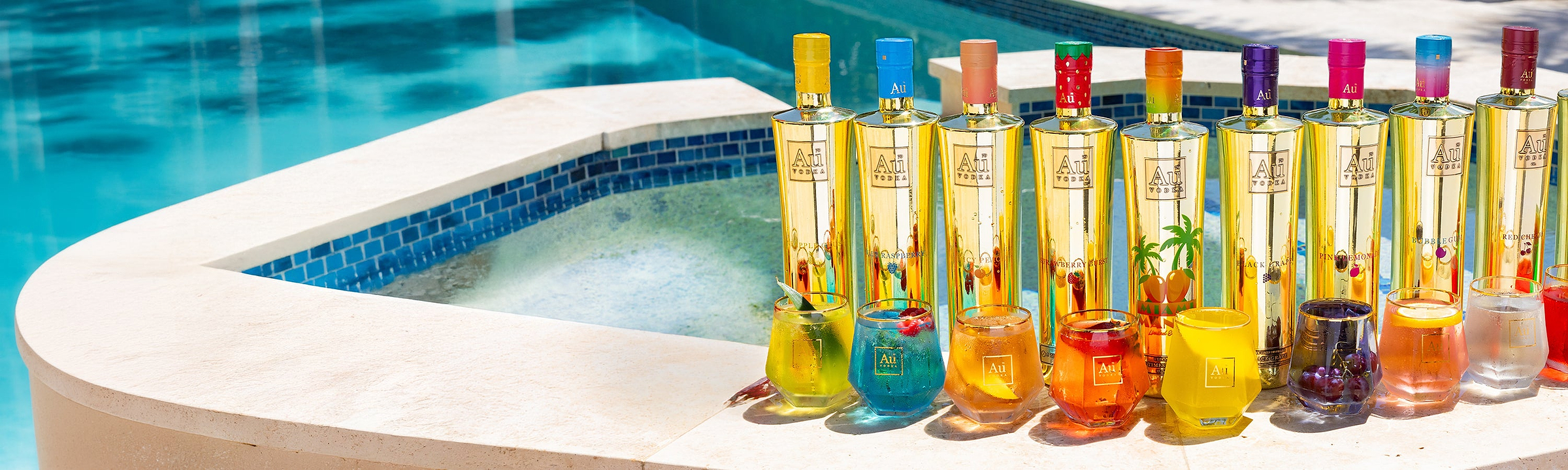 Au Vodka bottles in various flavors with matching cocktails by a pool