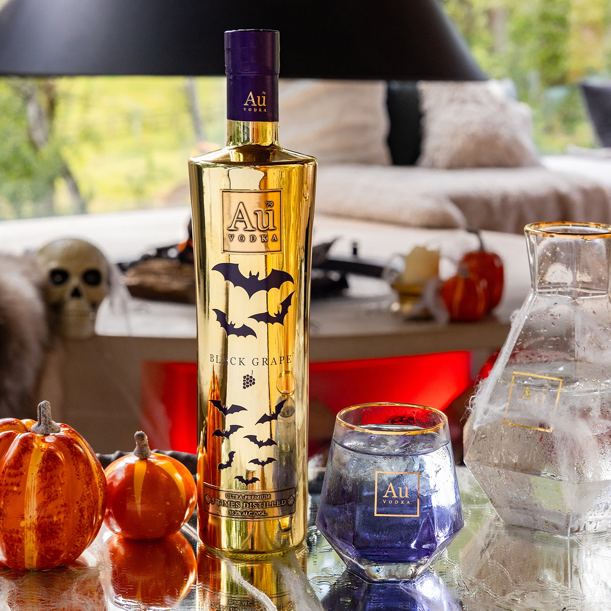 Au Vodka Black Grape bottle with bat graphics next to a glass of purple liquid and Halloween pumpkins