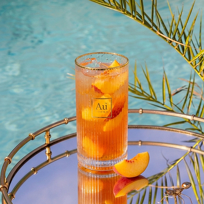 Au Vodka USA cocktail with peach slices and ice on a mirrored tray by a pool