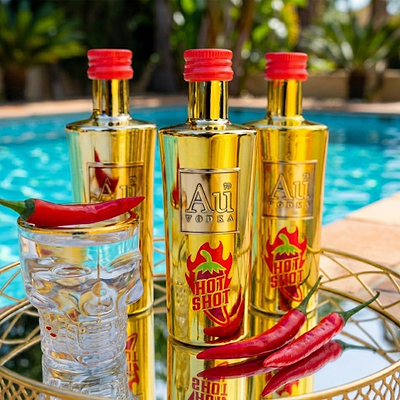 Three Au Vodka USA Hot Shot bottles and a skull-shaped glass with red chili peppers by a pool