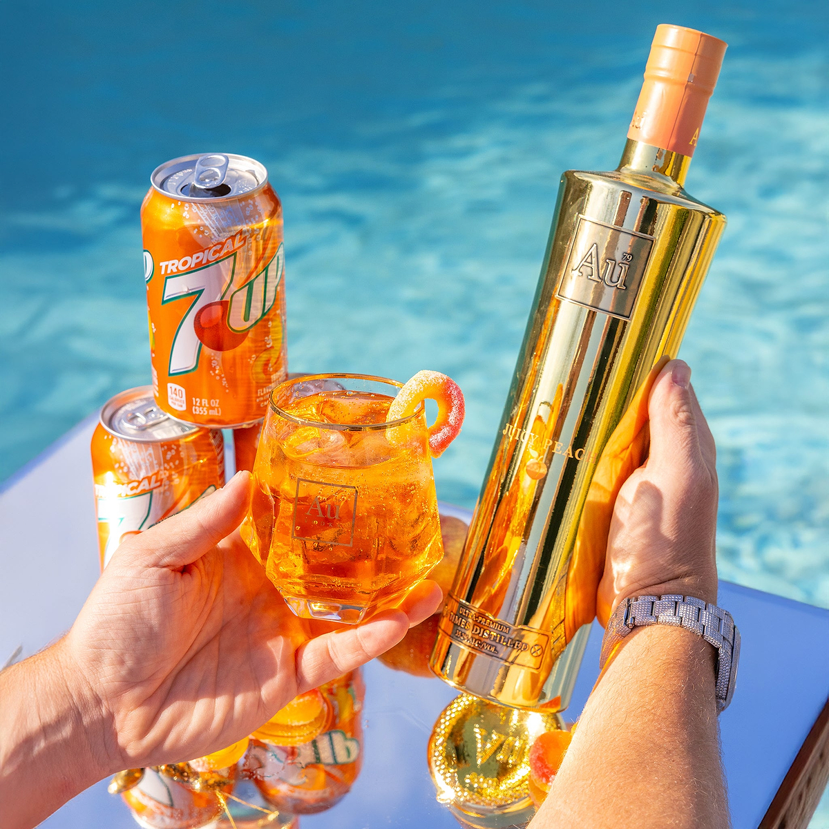 Au Vodka Juicy Peach bottle and cocktail with Tropical 7Up cans by a pool