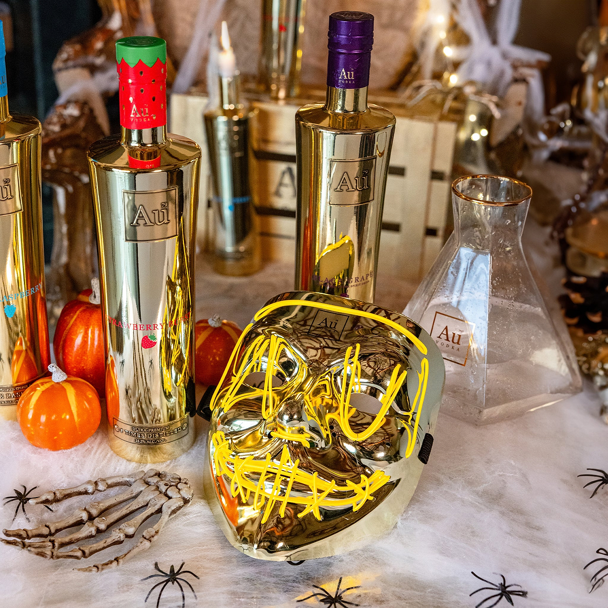 Au Vodka bottles with Halloween decorations including a gold mask and mini pumpkins