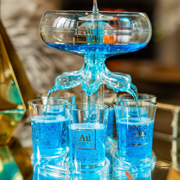 Au Vodka glass shot tower filled with blue liquid on a mirrored tray
