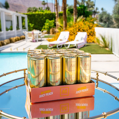 A 12-pack of Au Vodka USA Juicy Peach cans on a mirrored tray by a pool