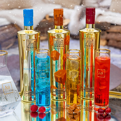 Three bottles of AuVodka with corresponding colored glasses on a reflective surface.