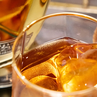 Amber liquid in a glass with a large ice cube next to a bottle