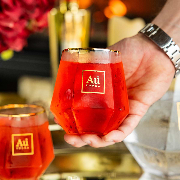Hand holding a faceted glass filled with red Au Vodka cocktail