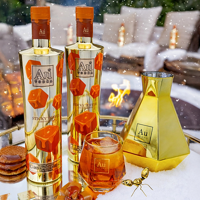 Two Au Vodka Sticky Toffee bottles and a glass of amber liquid on a snowy tray