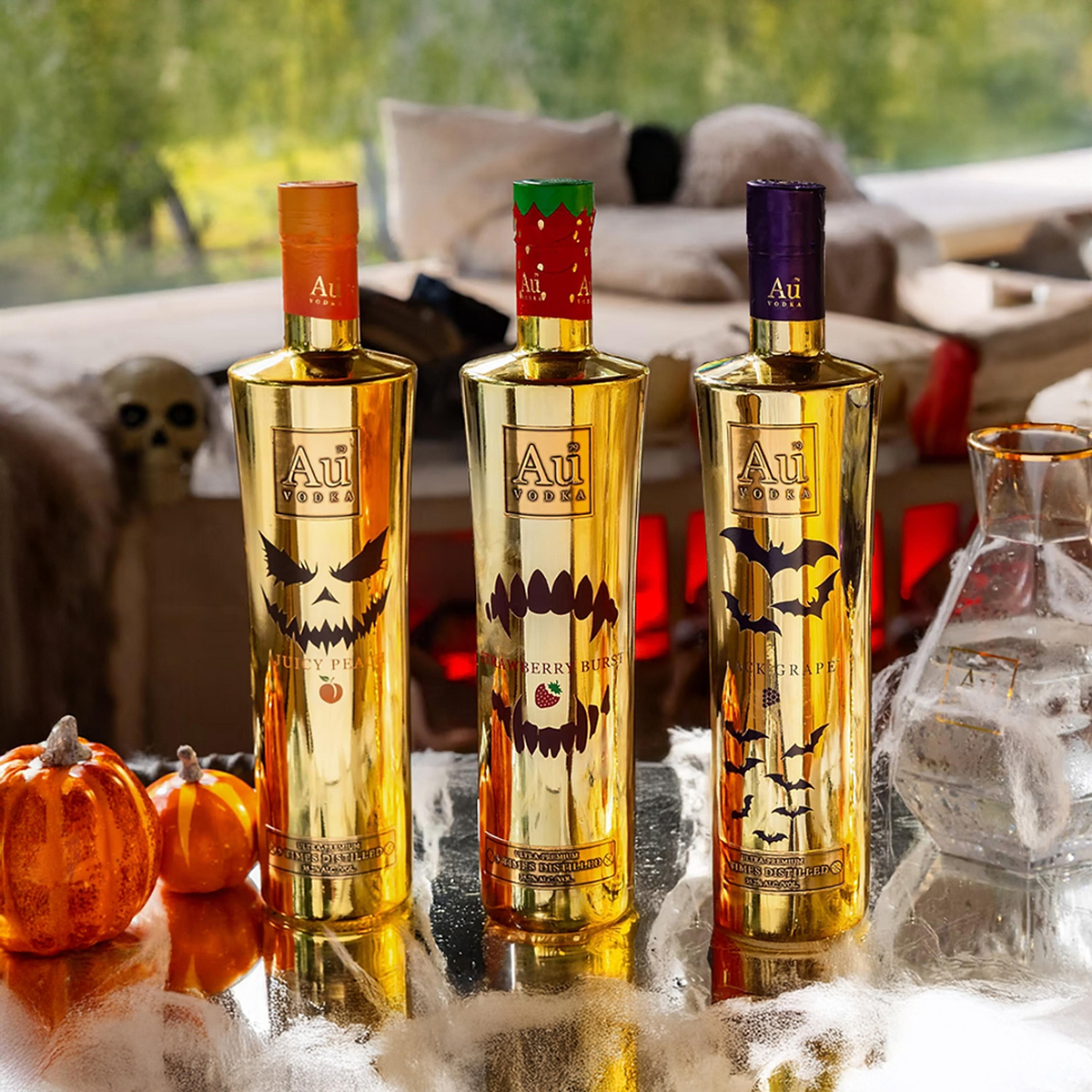Three Au Vodka bottles with Halloween themed designs on a reflective surface with pumpkins and cobwebs