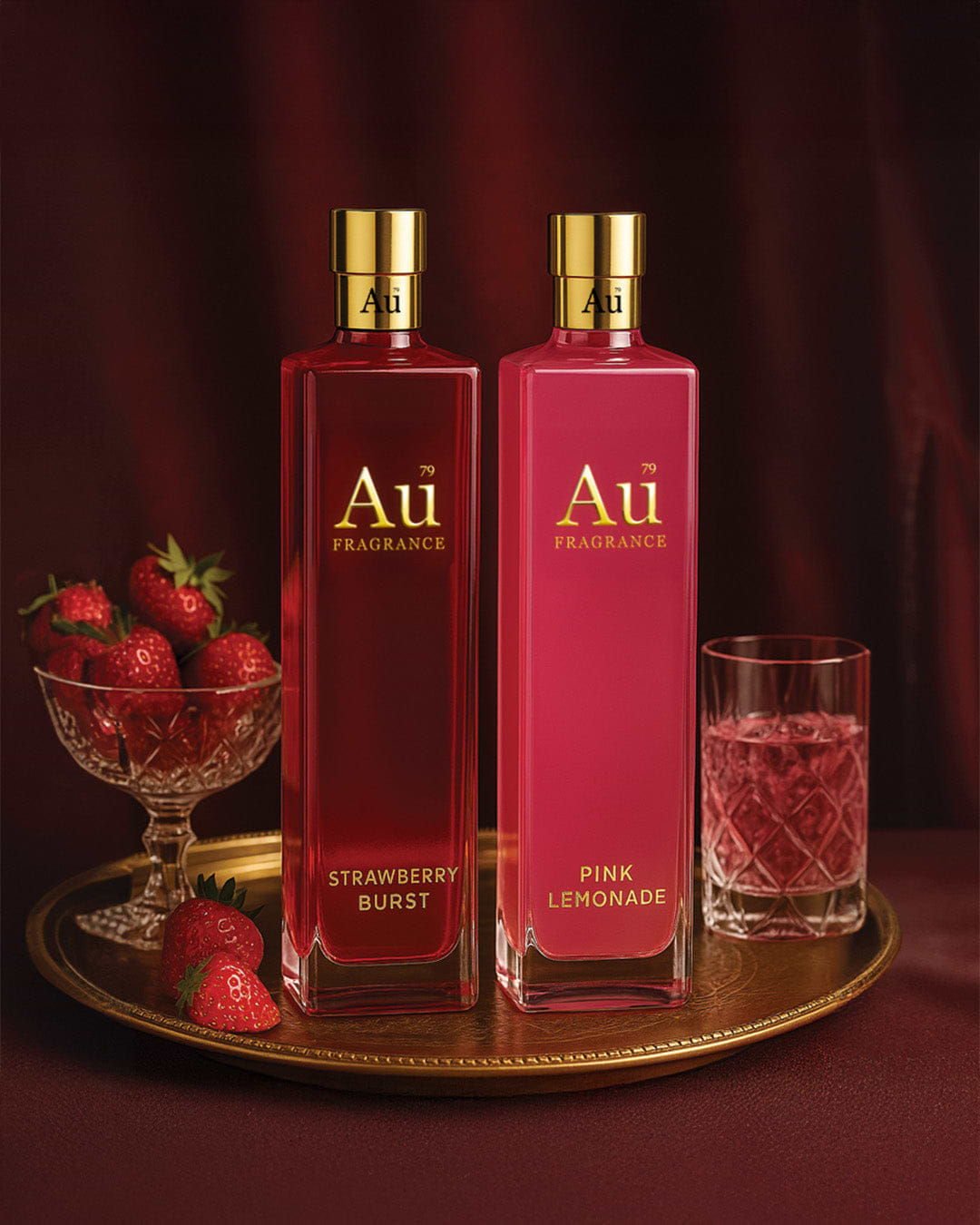 Au Fragrance Strawberry Burst and Pink Lemonade bottles on a gold tray with fresh strawberries and a glass