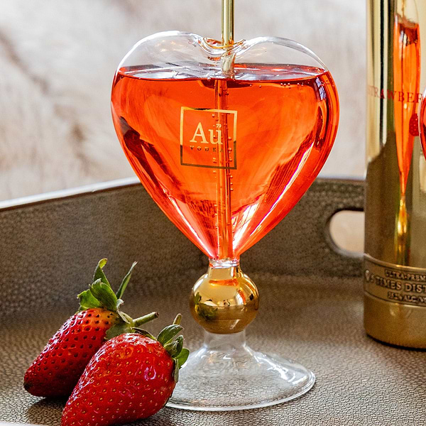 Au Vodka heart shaped glass filled with red liquid next to fresh strawberries on a tray