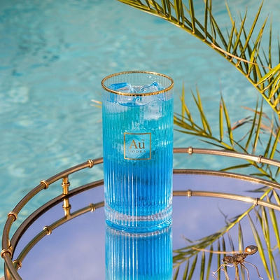 Au Vodka Blue Raspberry in a tall glass with ice on a mirrored tray by a pool