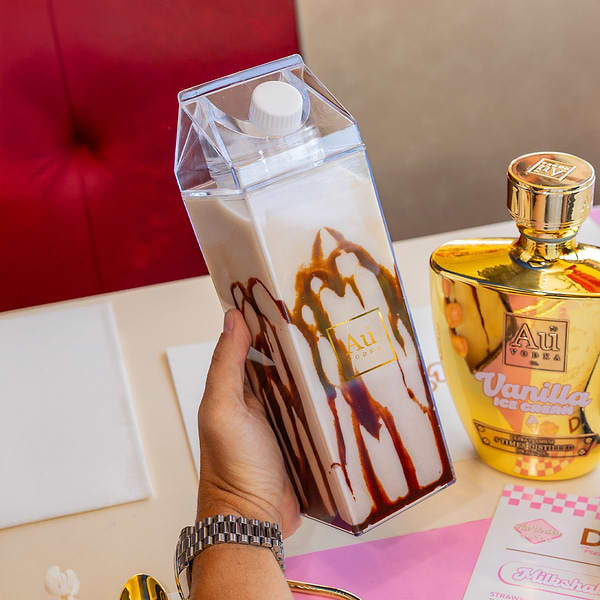 Hand holding a clear carton of chocolate drink next to a gold Au Vodka bottle