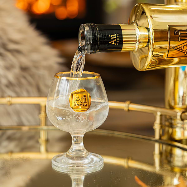Au Vodka being poured from a gold bottle into a branded Au Vodka glassware snifter
