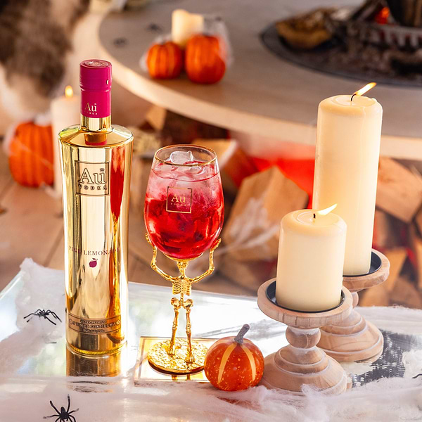 Au Vodka Pink Lemonade bottle and skeleton stem glass with red cocktail surrounded by candles and pumpkins
