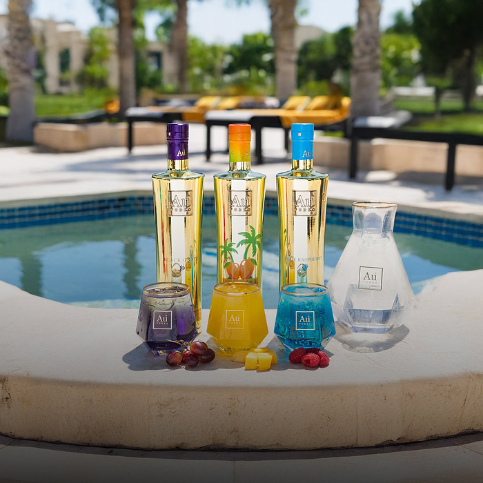 Three Au Vodka bottles and three glasses with fruit next to a pool