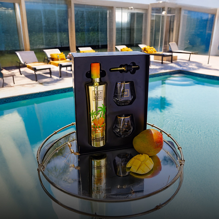 Au Vodka Miami Mango gift set with two glasses and a pourer, next to a mango, by a pool