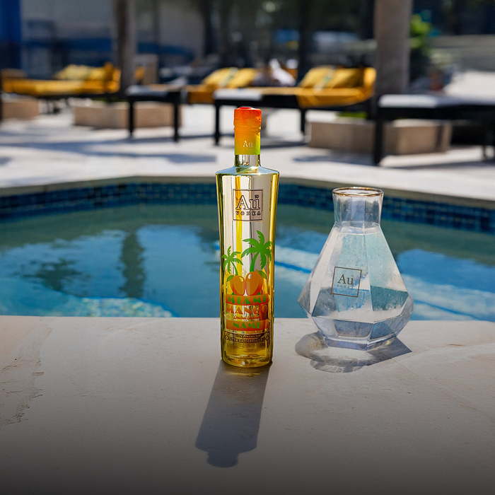 Au Vodka Miami Mango bottle and a glass decanter by a swimming pool