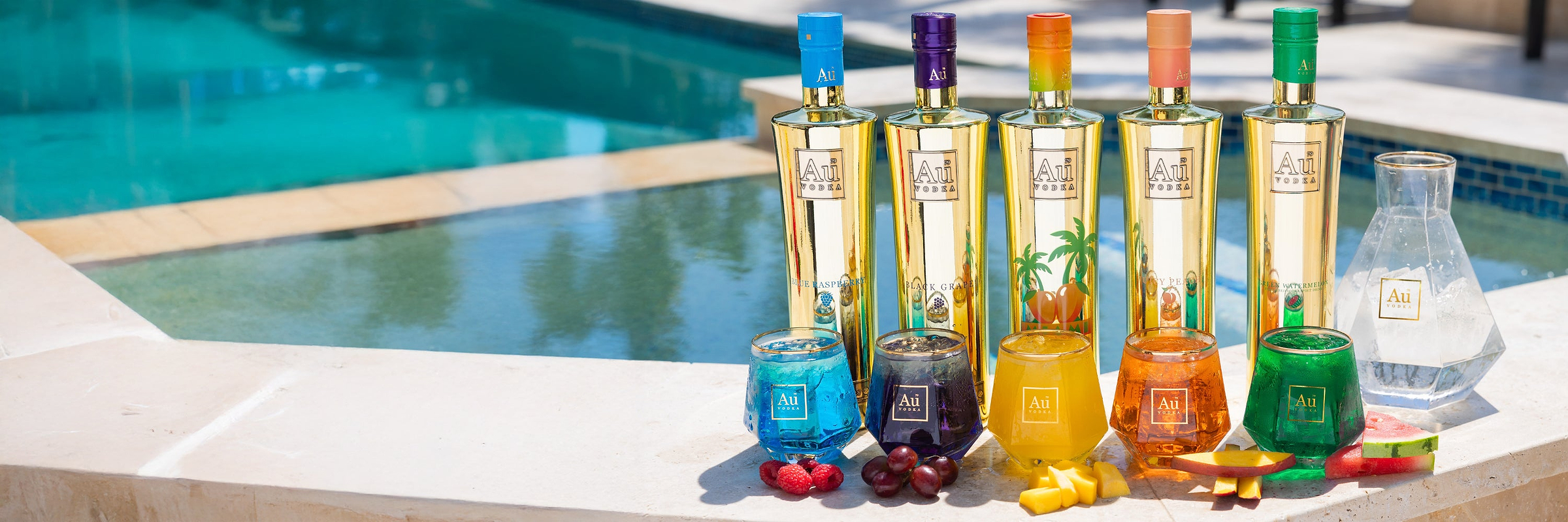 Five Au Vodka bottles and matching cocktails with fruit by a pool