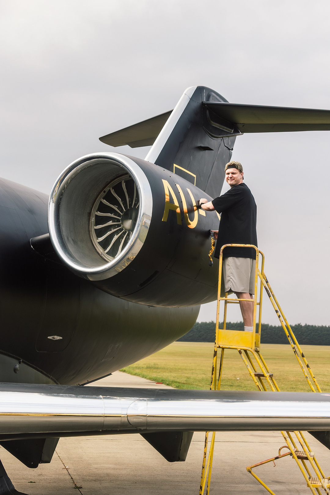 Man on a yellow ladder cleaning the gold lettering on the side of a black private jet engine